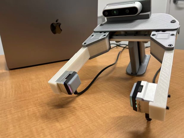 The hand-held gripper: UMI mechanics, two GelSight Mini sensors on modified fingers, and a RealSense D435 centred for a symmetric view.